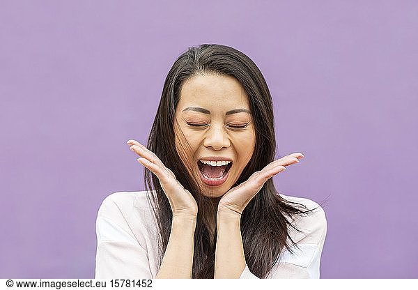 Porträt einer glücklichen Frau mit geschlossenen Augen  die vor violettem Hintergrund vor Freude weint