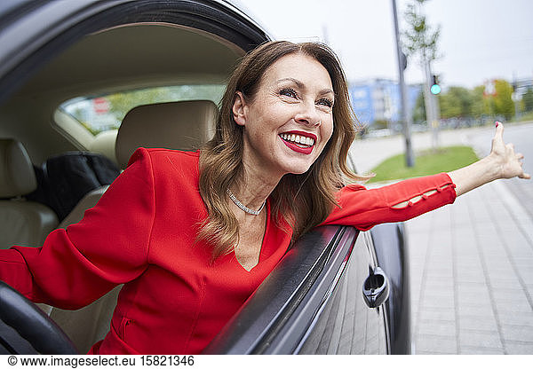 Porträt einer glücklichen reifen Frau  die sich aus dem Autofenster lehnt
