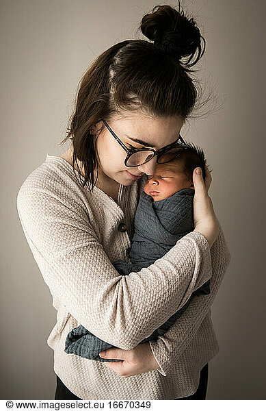 Porträt einer Hipster-Millennial-Mutter  die ihren neugeborenen Sohn wickelt und kuschelt