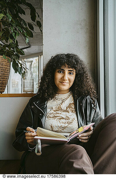 Porträt einer jungen Frau  die mit einem Buch an der Universität sitzt