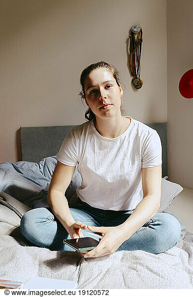 Porträt einer jungen Frau  die zu Hause auf dem Bett sitzt