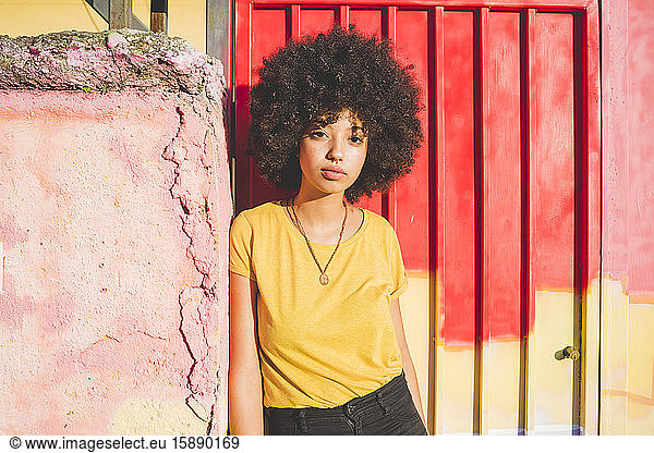 Porträt einer jungen Frau mit Afrofrisur  die an einer Wand lehnt