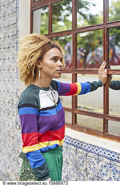 Porträt einer jungen Frau mit Afrofrisur  die sich an ein Spiegelfenster lehnt