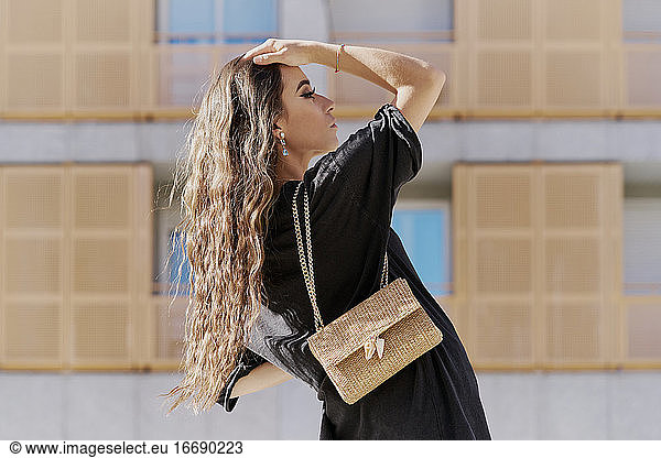Porträt einer jungen Frau mit lockigem blondem Haar und einer braunen Handtasche