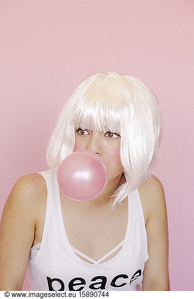 Porträt einer jungen Frau mit rosa Kaugummiblase vor rosa Hintergrund