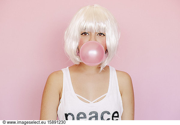 Porträt einer jungen Frau mit rosa Kaugummiblase vor rosa Hintergrund