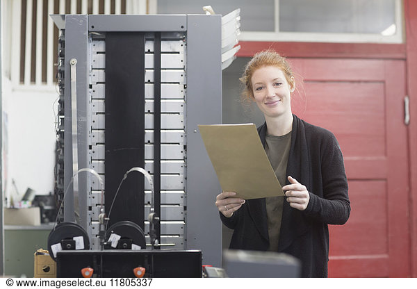 Porträt einer lächelnden Frau  die an einer Druckmaschine steht und ein Dokument hält
