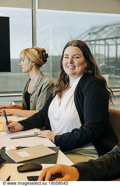 Porträt einer lächelnden Geschäftsfrau  die mit Kollegen am Schreibtisch in einem Coworking-Büro sitzt