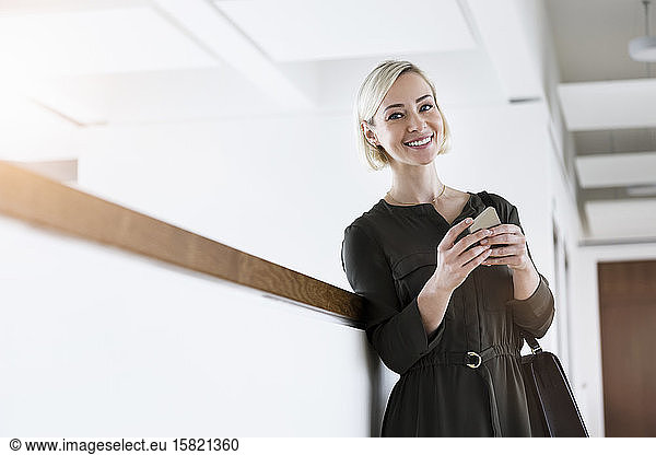 Porträt einer lächelnden Geschäftsfrau mit Mobiltelefon und Handtasche