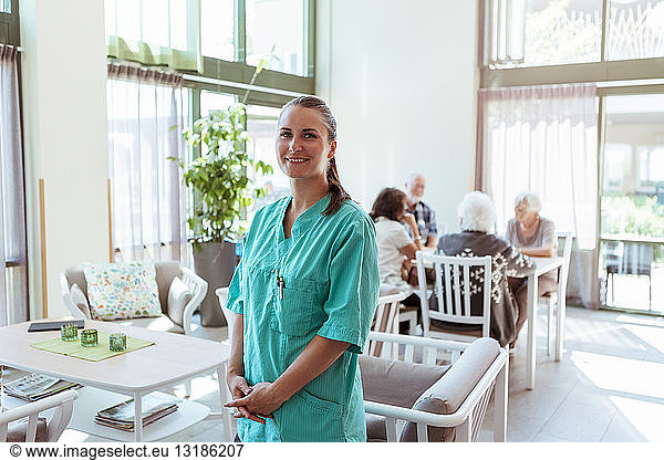Porträt einer lächelnden Gesundheitshelferin mit älteren Menschen im Hintergrund in einem Pflegeheim