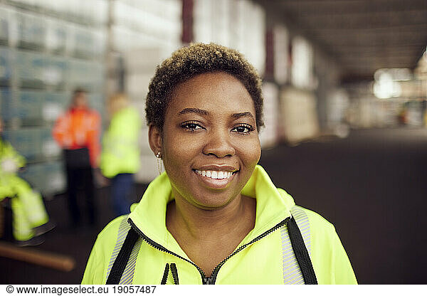 Porträt einer lächelnden jungen Arbeiterin in reflektierender Kleidung in der Industrie