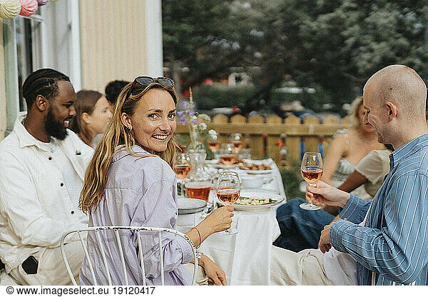 Porträt einer lächelnden jungen Frau  die über die Schulter schaut  während sie mit Freunden bei einer Dinnerparty im Café sitzt