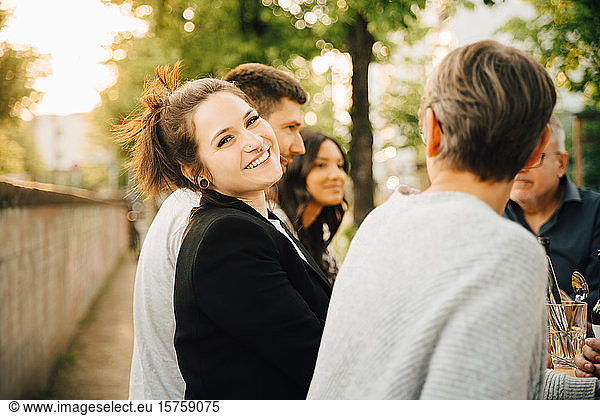 Porträt einer lächelnden jungen Frau  die mit Freunden zusammensitzt und sich am geselligen Beisammensein erfreut