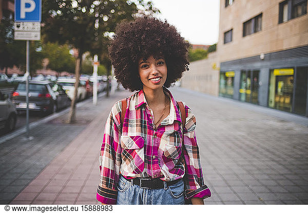 Porträt einer lächelnden jungen Frau mit Afrofrisur in der Stadt