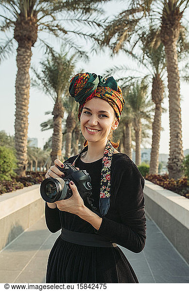 Porträt einer lächelnden jungen Frau mit Kopfbedeckung  die ihre Kamera hält