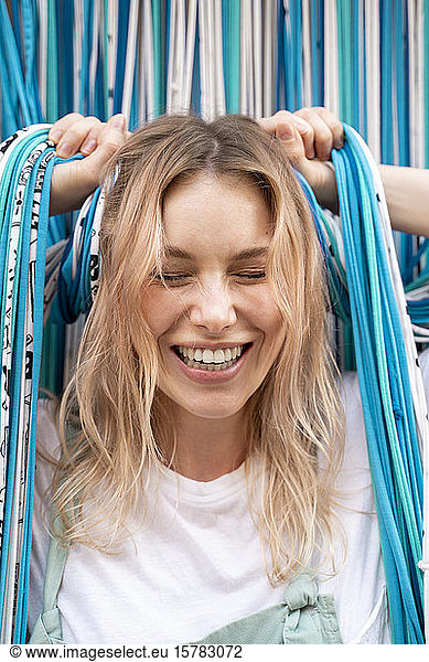 Porträt einer lachenden blonden Frau  die Fäden eines Türvorhangs hält