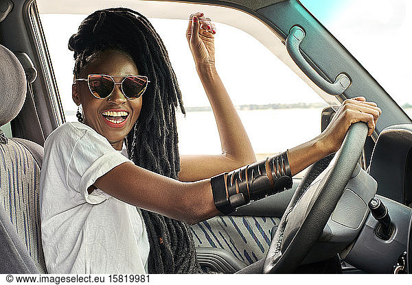 Porträt einer lachenden Frau mit Dreadlocks beim Autofahren