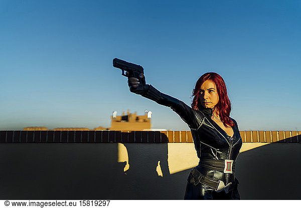 Porträt einer rothaarigen Frau mit Waffe in der Hand im schwarzen Ledercatsuit auf dem Dach