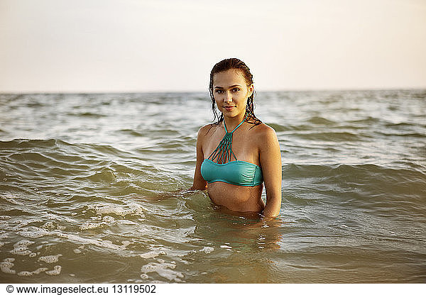 Porträt einer selbstbewussten Frau in blauem Bikini-Oberteil  die im Meer steht
