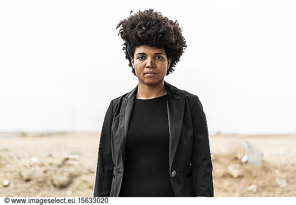 Porträt einer selbstbewussten  schwarz gekleideten jungen Frau in trostloser Landschaft