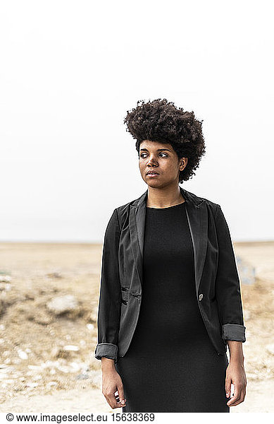 Porträt einer selbstbewussten  schwarz gekleideten jungen Frau in trostloser Landschaft stehend