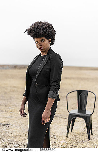 Porträt einer selbstbewussten  schwarz gekleideten jungen Frau in trostloser Landschaft stehend