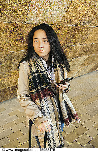 Porträt einer seriösen jungen Geschäftsfrau mit Smartphone und Trolley-Tasche