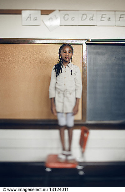 Porträt eines auf einem Stuhl stehenden Mädchens vor einer Tafel im Klassenzimmer