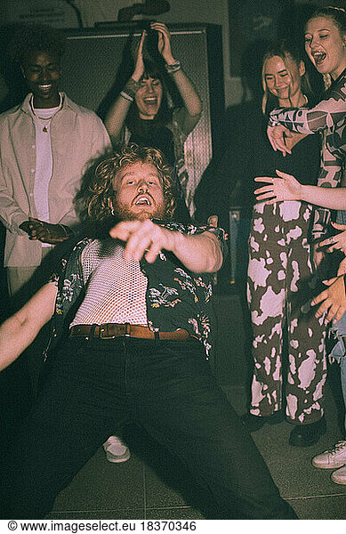 Porträt eines biegsamen jungen Mannes  der sich nach hinten beugt und inmitten von Freunden in einem Nachtklub tanzt