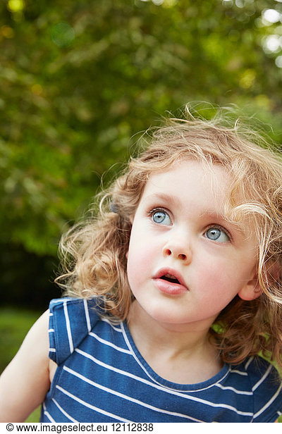Porträt eines blonden  gewellten Mädchens mit blauen Augen  das in einen Park blickt