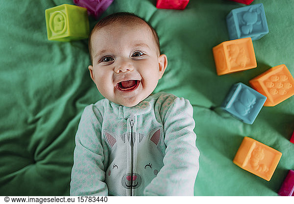 Porträt eines fröhlichen Mädchens auf grüner Matte liegend mit Gummispielzeug