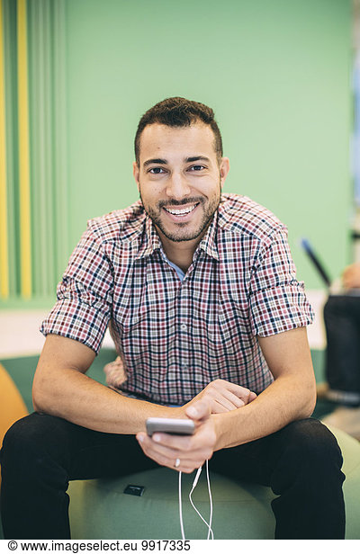 Porträt eines glücklichen Geschäftsmannes  der ein Smartphone in der modernen Bürolobby hält.