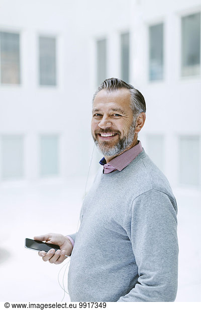 Porträt eines glücklichen Geschäftsmannes  der Musik über ein Smartphone im Büro hört.
