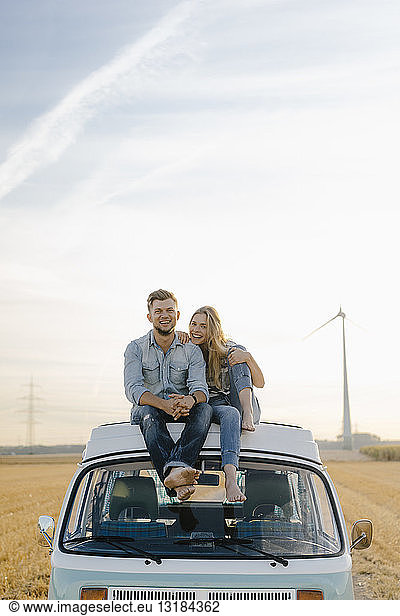 Porträt eines glücklichen jungen Paares auf dem Dach eines Wohnmobils in ländlicher Landschaft