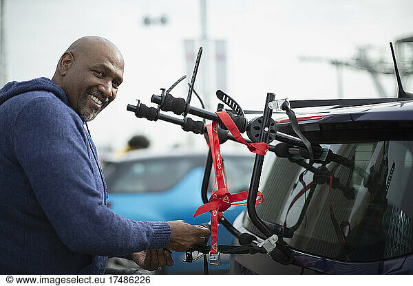 Porträt eines glücklichen Mannes am Fahrradträger eines Autos