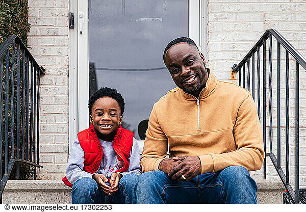 Porträt eines glücklichen Vaters und eines Sohnes  die am Eingang eines Hauses sitzen