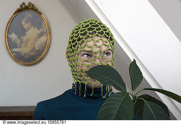Porträt eines jugendlichen Mädchens mit Avocadopflanze mit gehäkelter grüner Kopfbedeckung