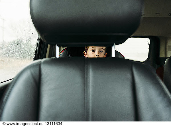 Porträt eines Jungen  der durch den Fahrzeugsitz schaut