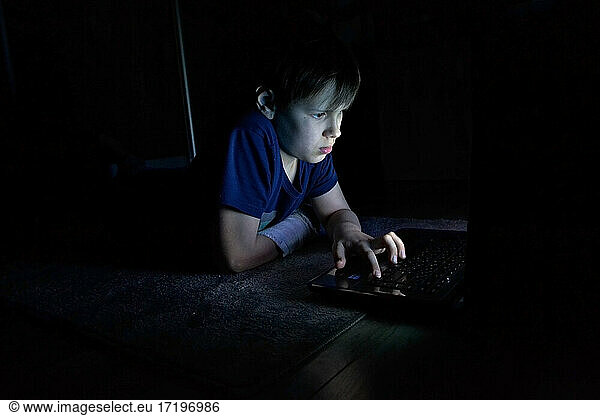 Porträt eines Jungen mit Laptop in einem dunklen Raum