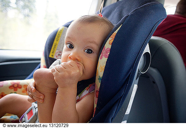 Porträt eines kleinen Mädchens  das in den Fuß beißt  während es auf einem Autositz sitzt