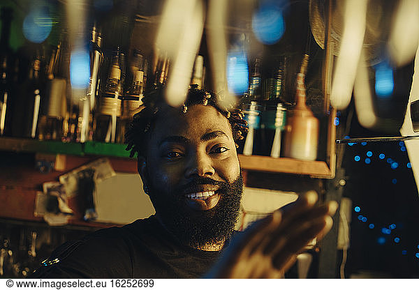 Porträt eines lächelnden Barkeepers mit Afro-Frisur bei beleuchteter