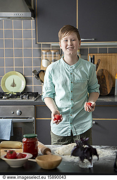 Porträt eines lächelnden Jungen  der in der Küche mit Tomaten jongliert