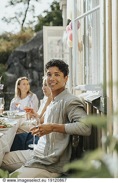 Porträt eines lächelnden jungen Mannes mit einem Weinglas in der Hand während einer Dinnerparty im Café