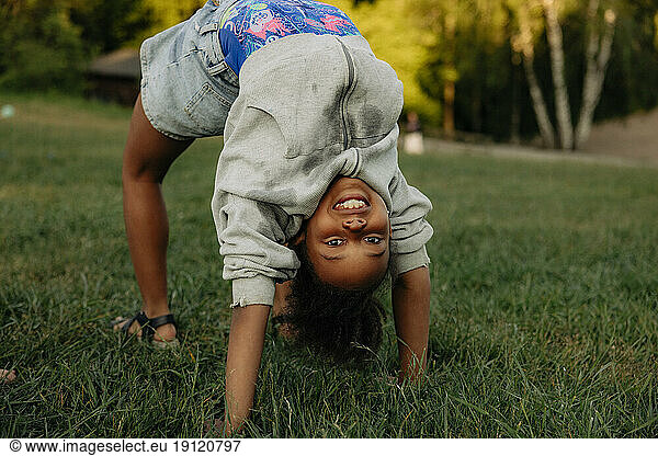 Porträt eines lächelnden Mädchens  das auf einem Spielplatz im Gras die Brückenstellung übt