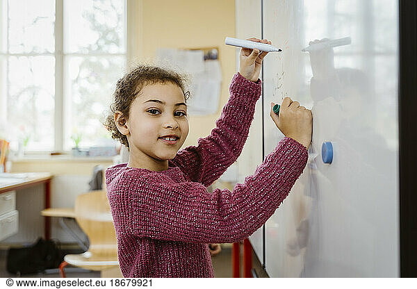 Porträt eines lächelnden Mädchens  das auf einer Tafel im Klassenzimmer schreibt