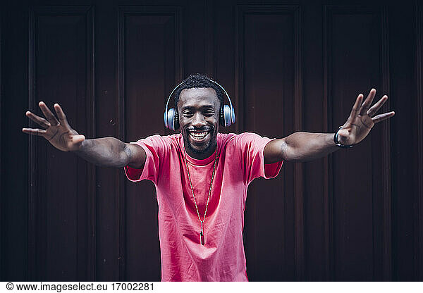 Porträt eines lachenden Mannes mit rosa T-Shirt  der mit Kopfhörern Musik hört