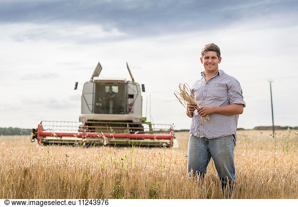 Porträt eines Landwirts  der eine Garbe Bio-Gerste auf dem Feld hält