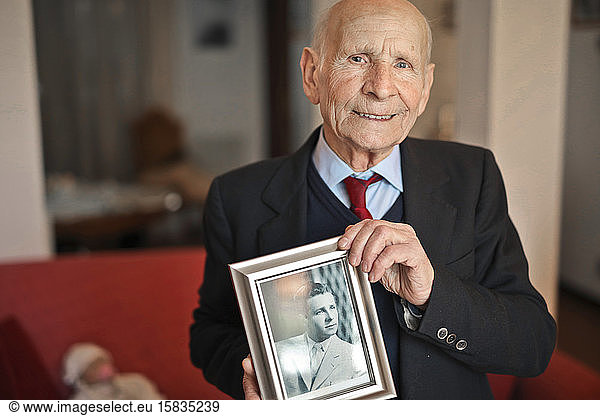 Porträt eines älteren Mannes mit einem Erinnerungsfoto als junger Mann