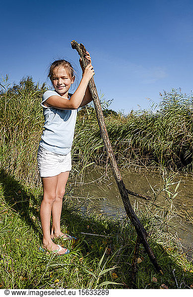 Porträt eines Mädchens mit einem Ast  das an einem Wasserlauf steht  Darß  Mecklenburg-Vorpommern  Deutschland