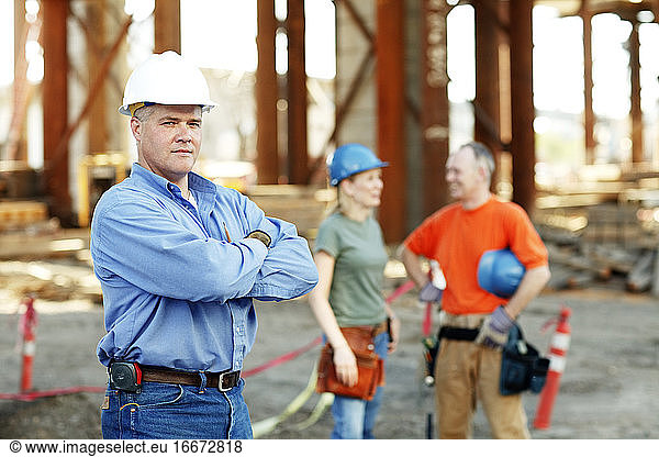 Porträt eines männlichen Bauführers mit zwei Arbeitern dahinter